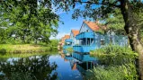 Reihe von sanierten Häusern am Ufer, als Teil des BEECH Resort Fleesensee, mit Spiegelung auf dem Wasser - symbolisch für innovative Kapitalanlagen in Ferienimmobilien